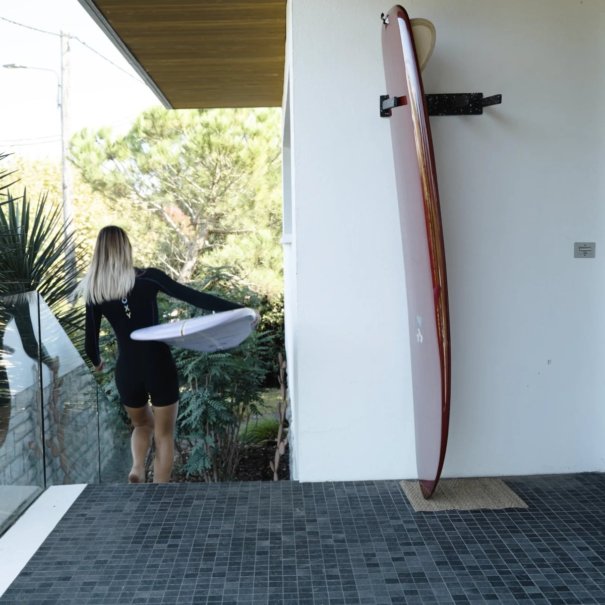 Rack de surf vertical EDERRAK en plastique recyclé avec un longboard rangé debout contre le mur